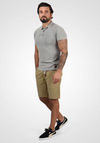 Cămașă polo gri cu mâneci scurte, pantaloni scurți kaki și adidași negri. Dispune de un guler și detalii din sfoară țesută pe pantaloni.