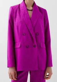 Blazer de corte cruzado en un vibrante fucsia, con un patrón texturizado y ondulado, solapas con muesca y dos bolsillos frontales con botones a juego.