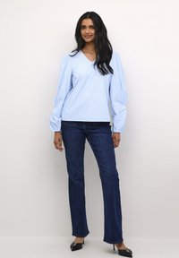 Blusa a righe azzurre con maniche lunghe a sbuffo, scollatura a V, abbinata a jeans blu scuro e décolleté nere a punta.