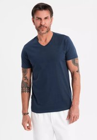 Námořnické bavlněné tričko s designem do V, krátkými rukávy a přiléhavým střihem. Výrazné tetování na pažích. Jednoduchá barva, hladká textura.