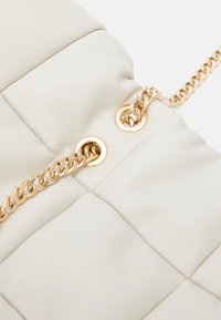 Puffed white leather handbag featuring a gold chain strap and circular hardware accents. Textured surface with quilted pattern.