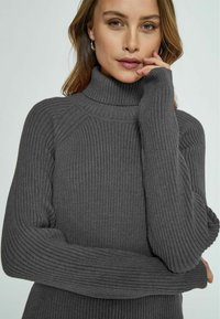 Gray ribbed turtleneck sweater with long sleeves and fitted design. Fabric has a soft texture, featuring subtle vertical lines and a high collar.