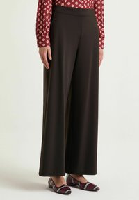 Pantaloni neri a gamba larga con texture liscia e vita elastica, abbinati a una camicetta bordeaux con fantasia e ballerine multicolor.