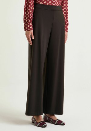 Black wide-leg trousers with a smooth texture and elastic waistband, paired with a patterned maroon blouse and multicolored flats.