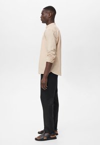 Beige long-sleeve shirt, black trousers, and black sandals. The shirt has a relaxed fit, buttoned cuffs, and a smooth texture.