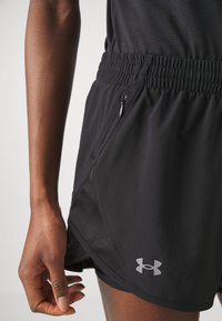 Mustat urheilushortsit, jotka on valmistettu kevyestä kankaasta ja joissa on verkkopaneeli sivussa, elastinen vyötärö ja pieni vetoketjullinen tasku.