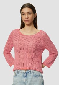 Rosa Strickpullover mit strukturiertem Design, weitem Rundhalsausschnitt und Dreiviertelärmeln, kombiniert mit hellblauen Jeans.