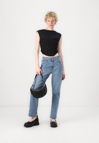 Top court noir à manches courtes, jean taille haute bleu clair, sac à main noir clouté et chaussures plates-formes noires massives.