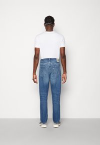 Ljusblå denimjeans med rak benpassform, som har en bakfickdesign och en etikett i midjan, bärs med en vit t-shirt.