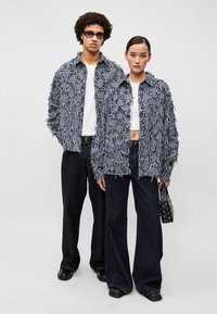 Divas divi modelis valkā atbilstīgas zilo un baltu svītru frēžotas jakas ar teksturētu dizainu virs baltām blūzēm, kombinētas ar brīvām tumšām džinsu biksēm.