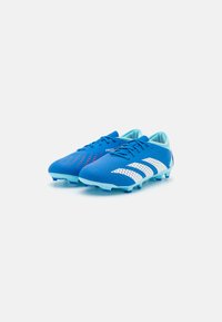 Des chaussures de soccer bleues avec une tige texturée, comportant des rayures blanches et de petites accents rouges. Conçues avec un matériau léger et respirant.
