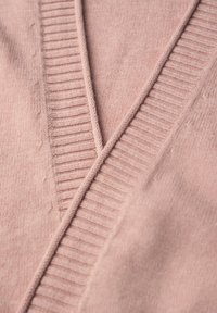 Ljusrosa tröja med V-ringning. Har ribbade accenter längs halslinningen. Mjuk textur med synliga stickade detaljer.