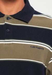 Polo shirt met een geribbelde textuur, voorzien van olijfgroene, marineblauwe en witte horizontale strepen. Inclusief twee knopen en een logo.
