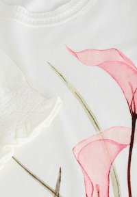 Bijela tkanina s cvjetnim uzorkom koja sadrži dizajne ružičastih ljiljana. Uključuje detalje na rukavima s nabranim i volanima. Mekana tekstura, lagani materijal.