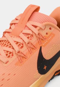 Pantofii de alergare Nike pentru trasee, de culoare roz corai, având un superior din plasă texturată, un swoosh negru contrastant și șireturi întărite pentru un fit sigur.