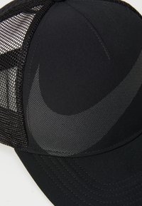 Fekete sapka hálós oldalakkal, elől nagy fekete logóval. Strukturált anyag és hajlított napellenző. Varrott részletek az illesztések mentén.
