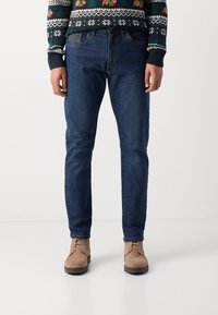 Donkerblauwe spijkerbroek met een tapered fit en vijf zakken, gecombineerd met beige veterschoenen. Geweven trui met een gestructureerd ontwerp en meerkleurige patronen.