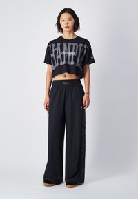 Camiseta negra corta con gran impresión de "CHAMPION"; combinada con pantalones negros holgados que presentan un detalle de logo delgado a los lados y cintura elástica.