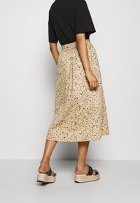 Béžová midi sukně s tečkovaným vzorem v modré, hnědé a černé barvě, s elastickým pasem; kombinována s černými platformovými sandály.