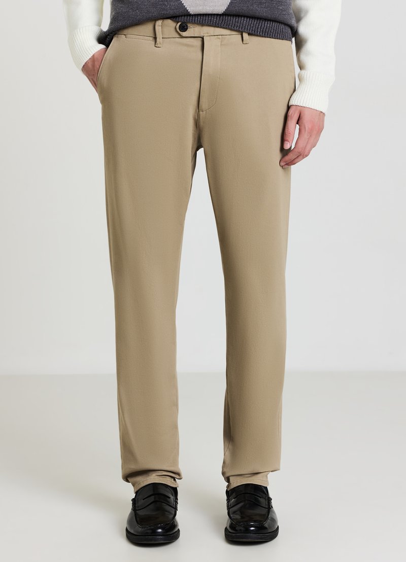 Pantaloni beige in tessuto liscio, con vestibilità classica, tasche frontali, chiusura con bottone, abbinati a scarpe eleganti nere.