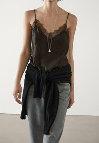 Mörkbrun satinkamisol med spetskant, kombinerad med grå jeans och en svart stickad tröja knuten runt midjan. Långt silverhalsband som accent.