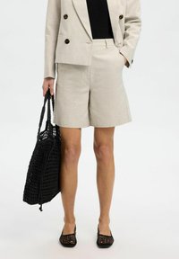 Pantaloni beige su misura con taglio dritto, tessuto testurizzato, abbinati a una borsa nera lavorata a maglia e ballerine nere in rete.