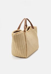 Beige vävd toteväska med texturerad yta och bruna läderhandtag, med en något fransig övre öppning för en avslappnad stil.