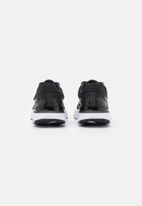 Scarpe sportive nere con tomaia in mesh, dettagli testurizzati sul tallone, midsole bianca e suola nera con motivo testurizzato.