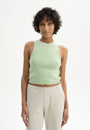 Light green ribbed knit crop top with a high neckline and sleeveless design, paired with beige relaxed-fit pants. Smooth texture.