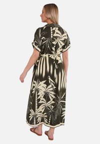 Robe maxi en tissu vert foncé ornée d'un motif floral et de feuilles de palmier crème, avec des manches courtes et une taille ceinturée pour un ajustement réglable.