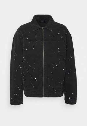 Schwarze Jeansjacke zum Reißverschluss mit weißem Farbklecks-Design, zwei Vorder Taschen und klassischem Kragen, vor einfarbigem Hintergrund dargestellt.