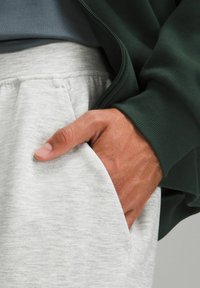 Grijze sweatpants met een textuurfinish en zijzakken, gecombineerd met een donkergroene ziptrui. Hand valt casual in de zak.