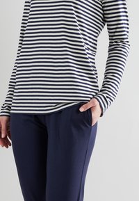 Top de rayas de manga larga en algodón azul marino y blanco, combinado con pantalones azul marino. La parte superior presenta rayas horizontales y un corte relajado.