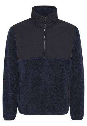 Tengerészeti kék bolyhos pulóver, fekete elülső panellel, magas nyakú és fél zippes záródással. Puha textúra és laza illeszkedés.