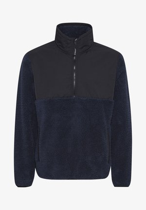 Tengerészeti kék bolyhos pulóver, fekete elülső panellel, magas nyakú és fél zippes záródással. Puha textúra és laza illeszkedés.