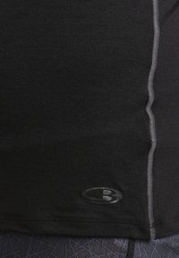 Svart tettsittende tanktop med grå sømmer, med en liten svart logo nederst til venstre, laget av et glatt, elastisk materiale.