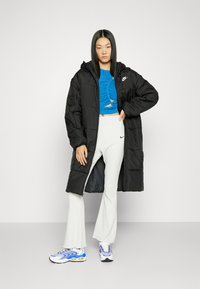 Melna pūkaina jaka ar kapuci, apvienota ar zilu īsu topu un baltām ribota stila platām biksēm. Sniegtas baltas un zilas kedas.