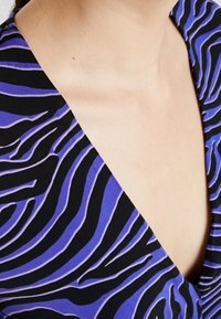 Kuvioitu toppi, jossa on V-kaulus ja mustia ja purppuranvärisiä seepra-raitoja, valmistettu sileästä, kevyestä kankaasta.