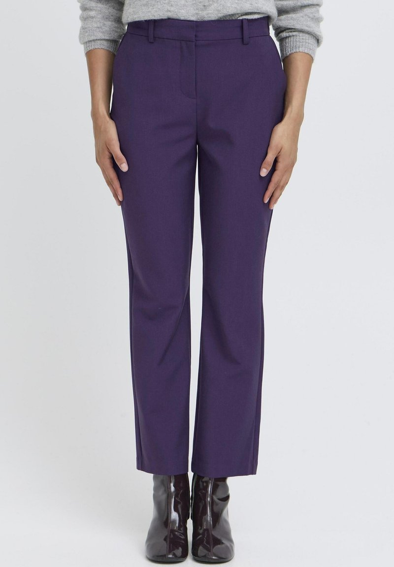 Pantalons taillés violets au toucher lisse, dotés de poches latérales et d'une coupe droite, accompagnés de bottines noires brillantes.