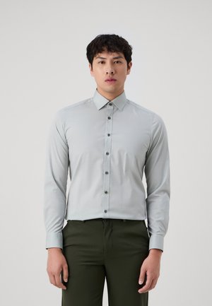Hellgraues Langarmhemd mit Button-Down-Kragen, das eine glatte Textur und dunkle Knöpfe aufweist, getragen mit dunkelgrünen Hosen.