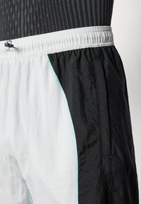 Laufshorts aus schwarzem und weißem Nylon mit glänzender Textur, elastischem Bund, Seitentaschen und hellblauen Nähakzenten.