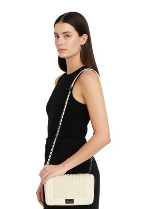 Donna con top nero senza maniche che tiene una borsa a tracolla bianca trapuntata con tracolla a catena su sfondo bianco.