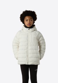 Μπουφάν puffer σε εκρού χρώμα, με κουκούλα, φερμουάρ μπροστά και ραμμένη σχεδίαση. Συνδυάζεται με μαύρα κολάν χωρίς εμφανή σχέδια.