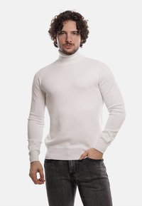 Maglione bianco a collo alto con un motivo testurizzato, design aderente e maniche lunghe, abbinato a jeans scuri. Stile semplice e moderno.