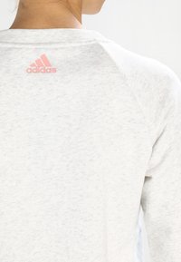 Primo piano della parte superiore della schiena di una persona che indossa una maglietta Adidas grigia chiara con un piccolo logo Adidas rosa vicino al colletto.