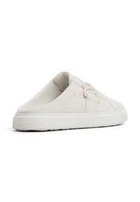 Weiße Canvas-Slipper mit einem strukturierten Seitenpanel, glattem Vorderteil, elastischem Riemen und einer Gummisohle. Minimalistisches Design ohne Verzierungen.