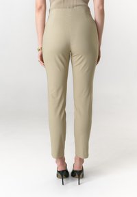 Beige, eng anliegende Hosen mit glatter Textur, hoher Taille, schmal zulaufenden Beinen und sichtbaren Nähten, kombiniert mit schwarzen Stiletto-Absätzen.