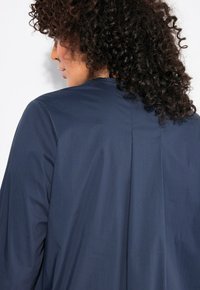 Marineblaue, leichte Jacke mit lockerer Passform, subtilen Nähten und einem Rückenfalten für zusätzliche Beweglichkeit. Glatte Textur und minimalistisches Design.