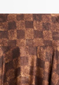 Tissu à carreaux marron avec une surface texturée, comportant des carrés alternant des teintes marron plus foncées et plus claires.