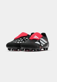 Μαύρα ποδοσφαιρικά παπούτσια με κόκκινες λεπτομέρειες και υφή στην επάνω πλευρά. Διαθέτουν έναν διακριτό σχεδιασμό με έντονες τρεις ρίγες και μορφοποιημένους στύλους.